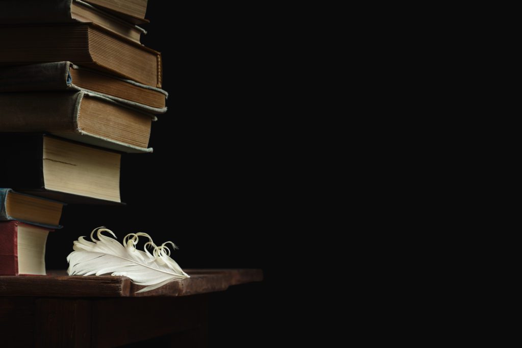 A photo of A stack of old books rises above a white feather